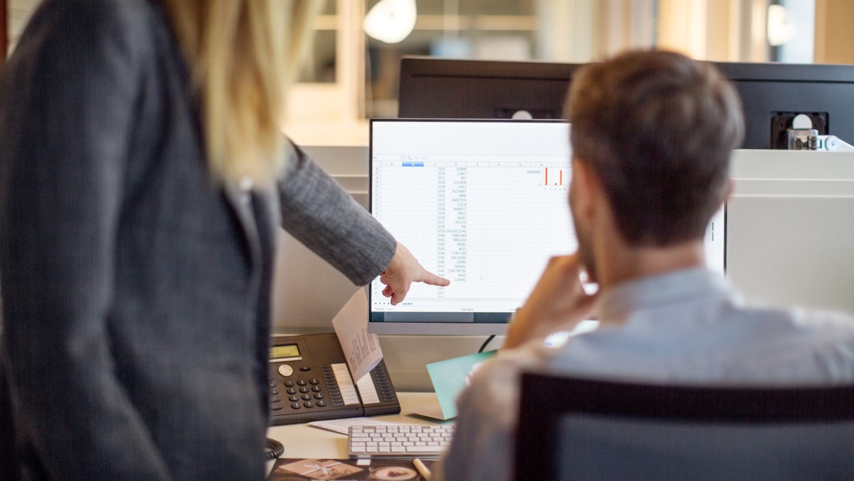 Woman and man in front of a monitor analyzing figures
