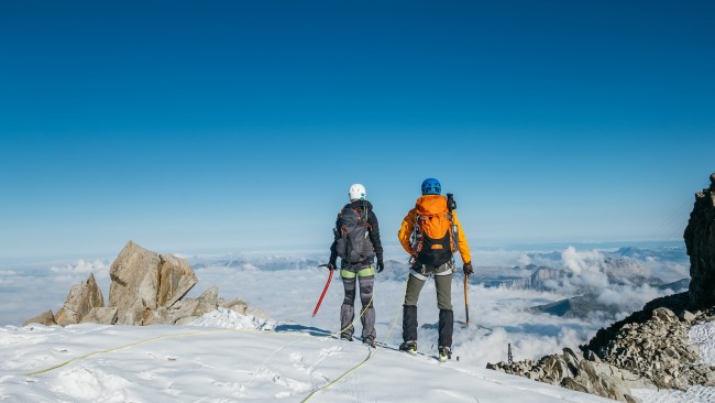 Rear view of two climbers in the snow above the clouds